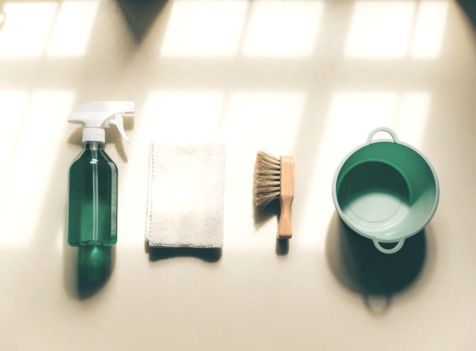 Spray bottle, cloth, brush and bucket laid out on a white surface