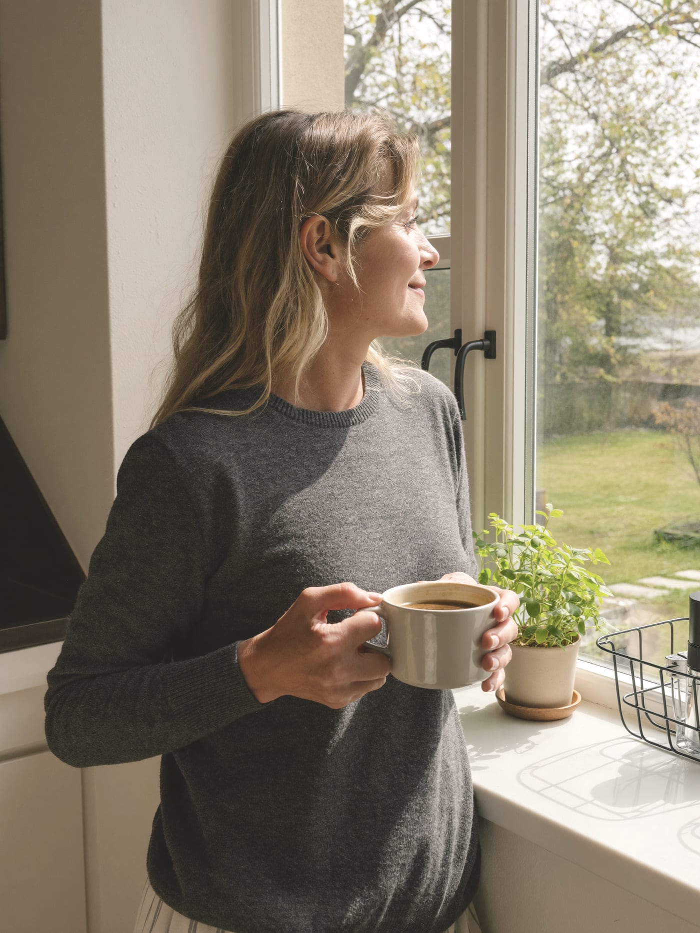 A woman with a mug looking out of a kitchen window