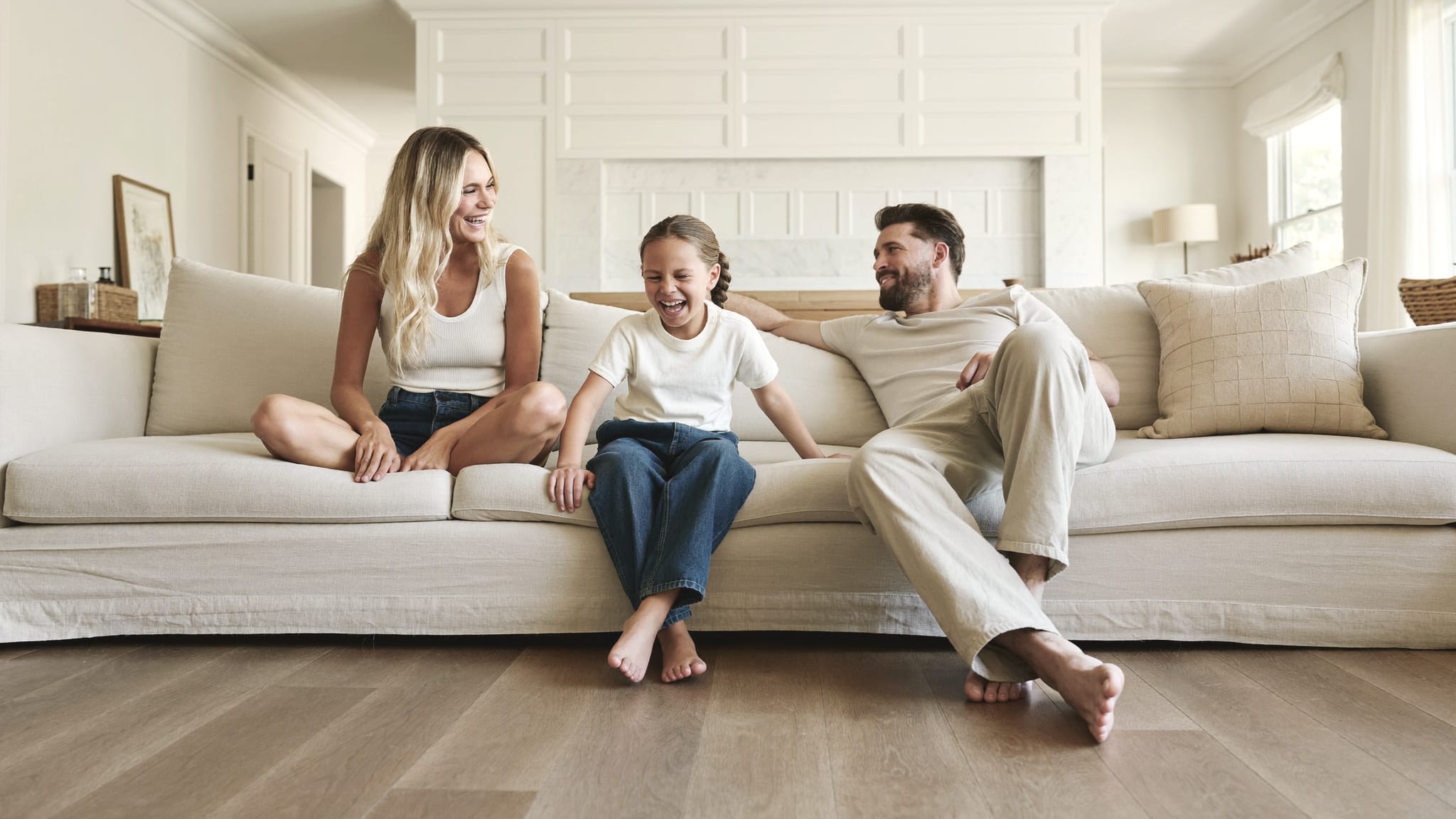 Parents and their daughter laughing together on a sofa in a bright, tidy living room