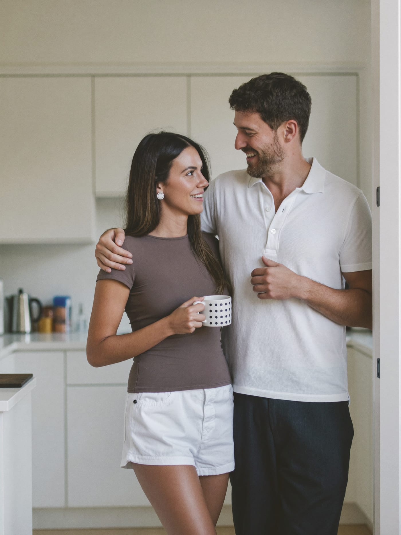 A couple standing together in a bright kitchen, holding mugs