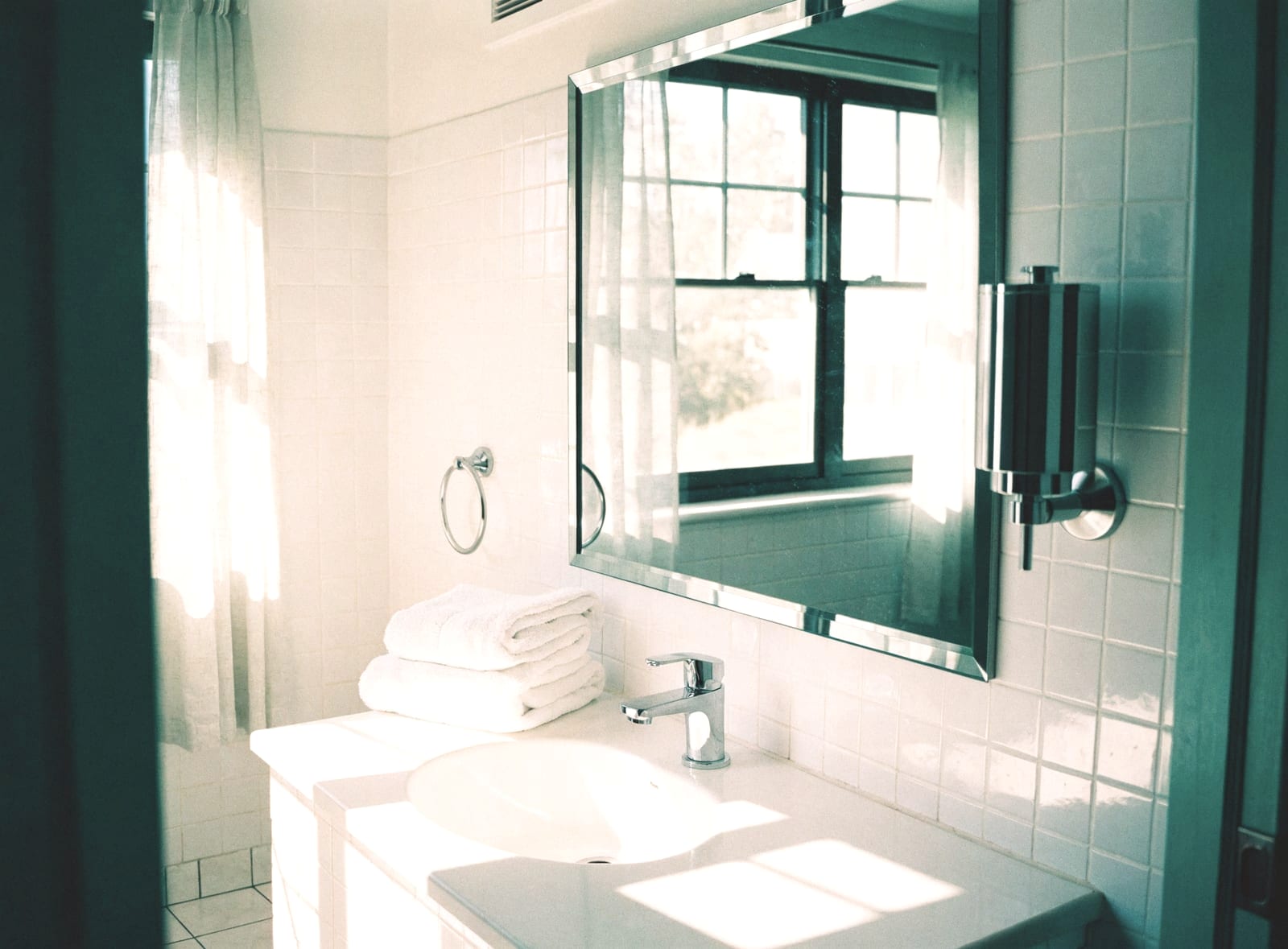 Spotless bathroom with white tiles, a mirror and folded towels