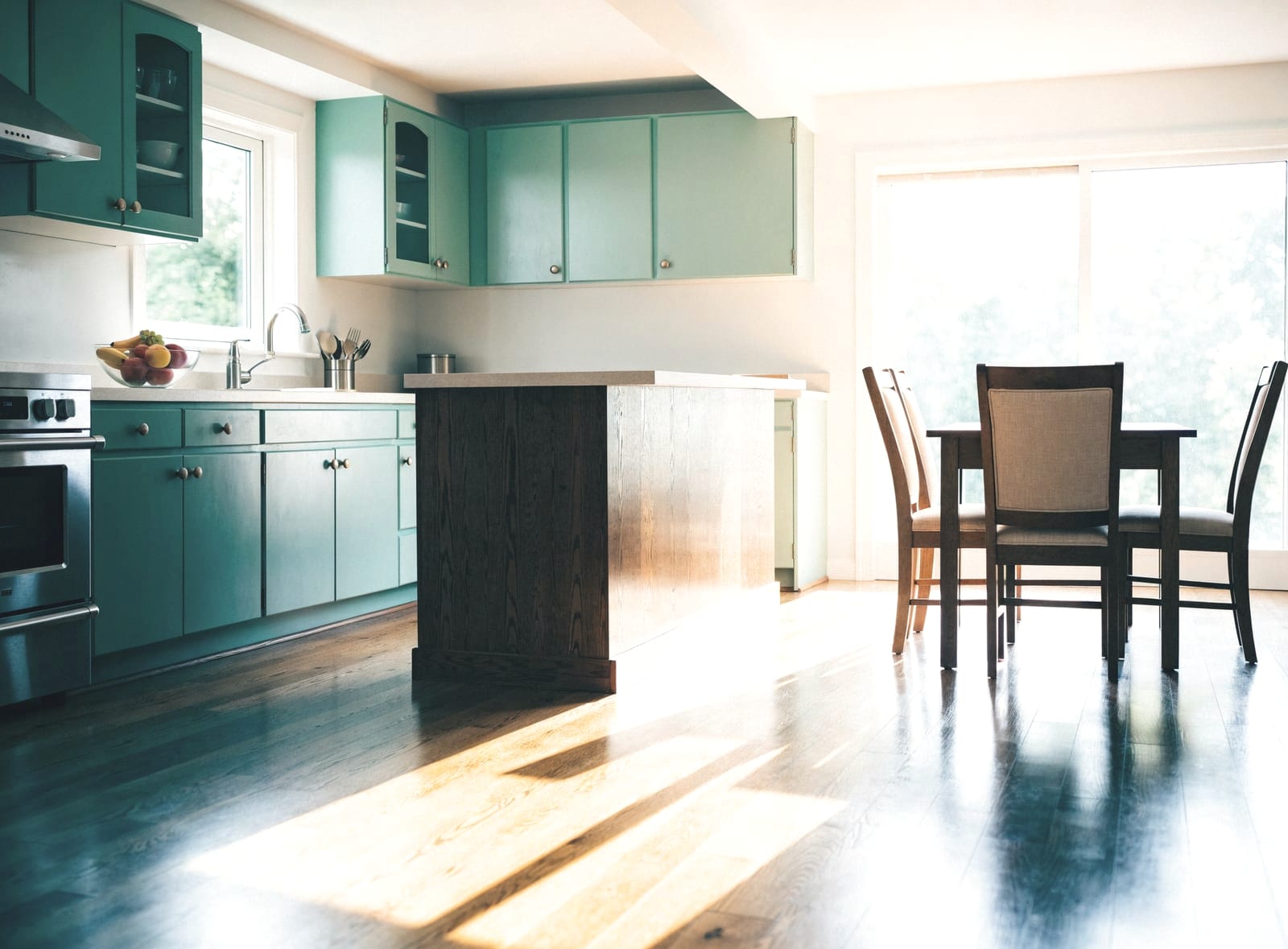 Clean kitchen with green cabinets, a dark island and a wooden dining table